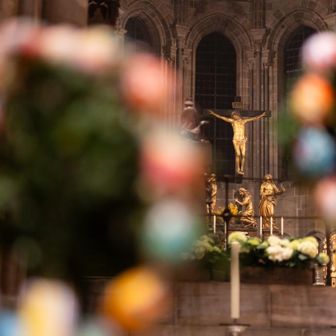 Das Bild zeigt die Kreuzigungsgruppe im Bamberger Dom, im Vordergrund ist Osterdekoration zu sehen.
